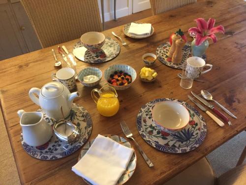 een houten tafel met borden, kopjes en keukengerei bij Brook Farm Cottage in Brackley