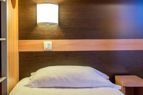 a bed with a wooden headboard with a light above it at Premiere Classe Annecy Nord - Epagny in Épagny