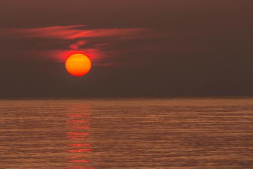 a red sun in the sky over the ocean at Sa Prata Hotel & Resort in Budoni