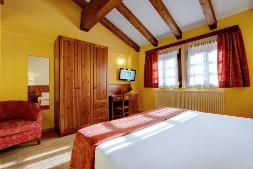 a bedroom with a bed and a chair and a television at iH Hotels Courmayeur Mont Blanc in Courmayeur