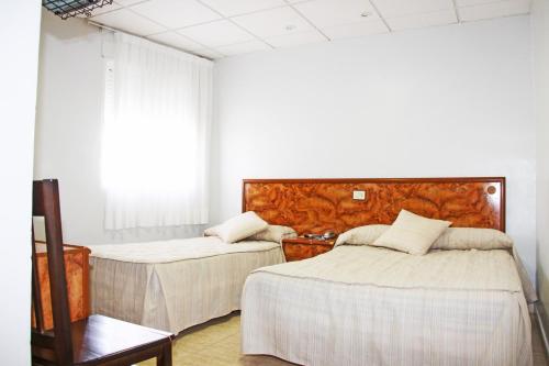 a bedroom with two beds and a chair at Hotel Trabuco in Santiago de la Ribera