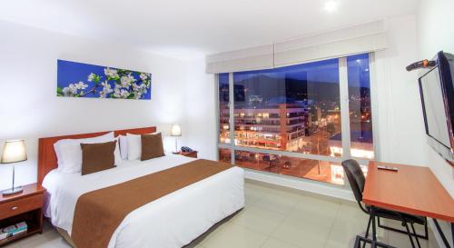 a bedroom with a bed and a desk and a window at 122 Plaza Apartahotel in Bogotá