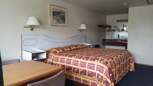 a hotel room with a bed, chair, table and lamp at Milwaukie Inn Portland South in Milwaukie