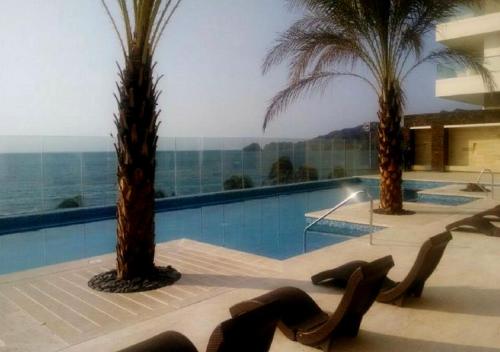una piscina con 2 palmeras y sillas en Apartamento Vacacional En Santa Marta Colombia frente a la Playa, en Santa Marta