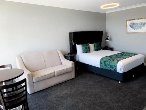 a bedroom with a bed and a chair and a table at Cascades Motor Inn in Dubbo