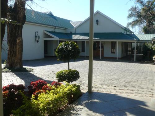 a white building with a tree and some flowers at Villa Jana Guesthouse in Pretoria