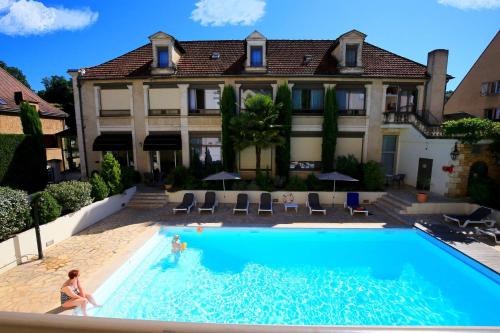 a woman standing in a swimming pool in front of a house at Hotel Le Renoir in Sarlat-la-Canéda
