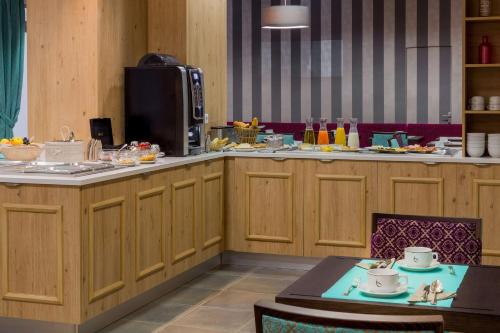 a kitchen with wooden cabinets and a table with cups on it at Hôtel Le Rive Droite & SPA in Lourdes