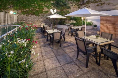 a patio with tables and chairs and umbrellas at Hôtel Le Rive Droite & SPA in Lourdes