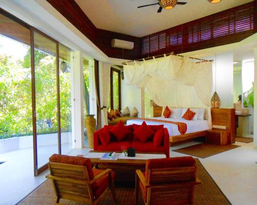a bedroom with a bed and a couch and chairs at Cahaya Indah Villas in Ubud