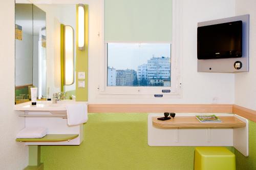 a bathroom with two sinks and a tv and a window at ibis budget Nancy Porte Sud in Houdemont