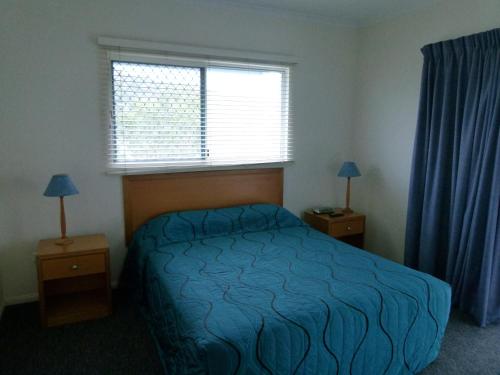 a bedroom with a bed with a blue comforter and a window at Madison Ocean Breeze Apartments in Townsville