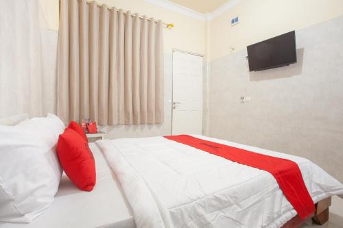een slaapkamer met een bed met rode kussens en een televisie bij RedDoorz Syariah At Sedati in Surabaya