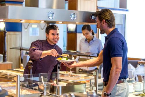 a man handing a man a plate of food in a kitchen at NOVAPARK Flugzeughotel Graz in Graz