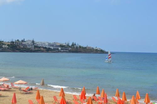 a beach with orange umbrellas and a sail boat in the water at 4S Beach Superior Apartments in Stalida