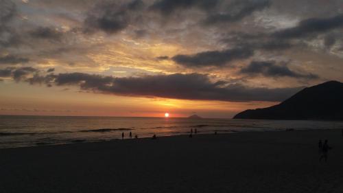 a sunset on the beach with people walking on the beach at Residencial Maresias Suites e Chalés in Maresias