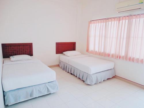 two beds in a white room with a window at Pakchong Phubade Hotel in Pak Chong