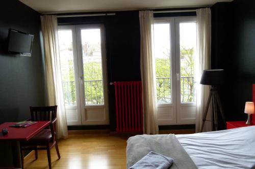 a bedroom with three windows and a bed and a desk at Hôtel Victor in Beauvais