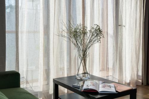 a vase of flowers on a table with a book at Elite Apartments Oliwa Martinique in Gdańsk