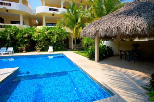 a swimming pool next to a hotel with a thatch roof at Las Turquezas in Puerto Escondido
