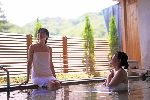 two women sitting in the water in a swimming pool at Hotel Hanamaki in Hanamaki