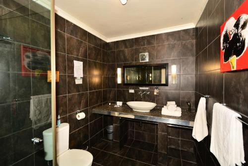 een badkamer met een wastafel, een toilet en een spiegel bij Secret Garden Guesthouse in Bloubergstrand