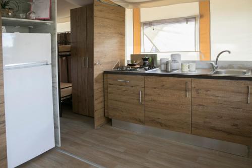 a kitchen with wooden cabinets and a white refrigerator at Ciriga Sicily Glamping in Santa Maria Del Focallo