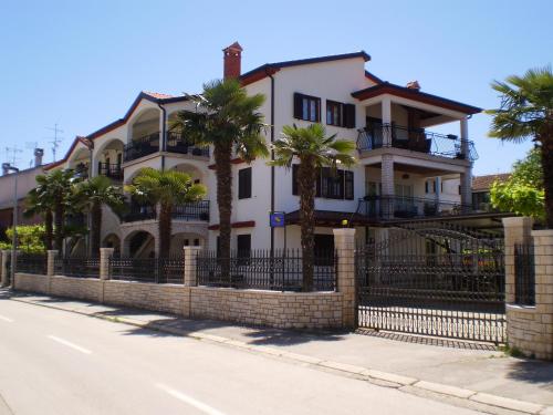 ein weißes Haus mit Palmen vor einem Zaun in der Unterkunft Apartments Modrušan in Rovinj
