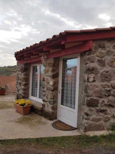 a stone building with a white door and a red roof at La maison D'Orée in Polignac