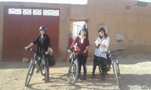 tres personas de pie con sus bicicletas delante de un edificio en Écologie oasis tafilalt CHEZ L' HABITANT, en Er Rachidia