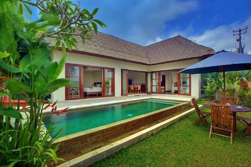 a house with a swimming pool and a table and an umbrella at Anusara Luxury Villas in Ubud