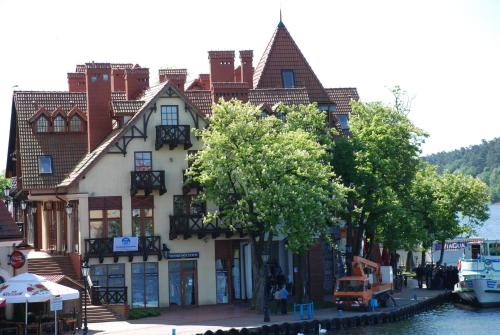 a building on the side of a river with trees at Mikołajki Apartamenty in Mikołajki