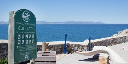 a sign in front of the ocean with a beach at Zzzone Boutique Hostel in Hermanus