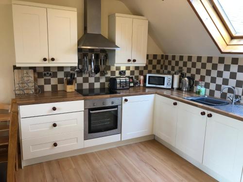 uma cozinha com armários brancos e um forno com placa de fogão em Hael Farm Cottage em Swansea