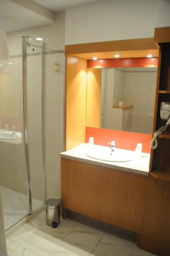 a bathroom with a sink and a shower with a mirror at Hotel Restaurant Au Parc des Cigognes in Kintzheim