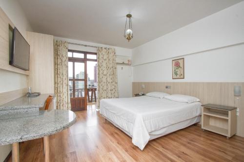 a bedroom with a white bed and a desk and a window at Alven Hotel by Slaviero Hotéis in Joinville