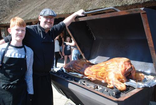 a man and a boy standing next to a grill with a turkey at Hytteby – Hanstholm Camping – Thy Feriepark in Hanstholm