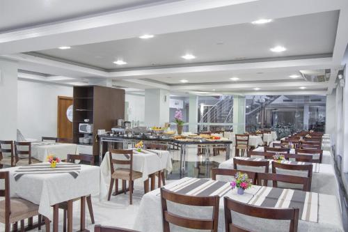 a restaurant with white tables and chairs and a kitchen at Alven Hotel by Slaviero Hotéis in Joinville