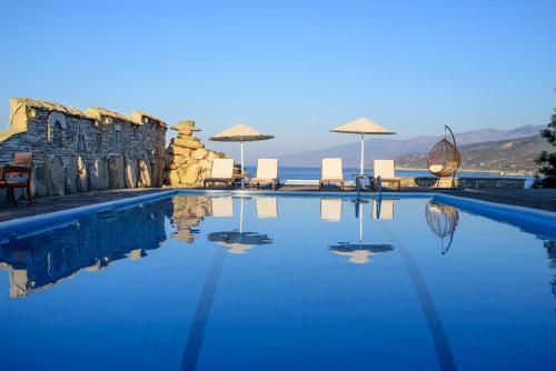 a swimming pool with chairs and umbrellas and the ocean at Cavos Bay Hotel & Studios in Armenistis