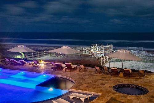 a pool with chairs and umbrellas on a beach at night at Bruno Marambaia Charme Hotel in Beberibe