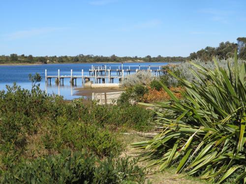 a dock on a body of water with plants at Lakes Entrance Waterfront Cottages with King Beds in Lakes Entrance