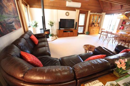 a living room with a brown leather couch with red pillows at Silverpoint Estate in Pokolbin