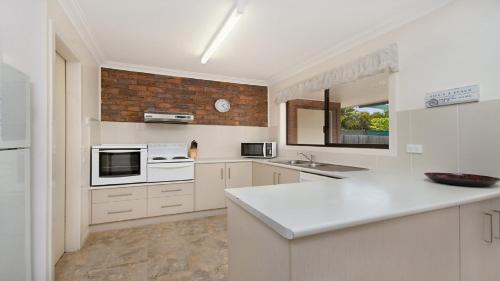 a kitchen with white cabinets and a brick wall at Alexander Palms in East Ballina