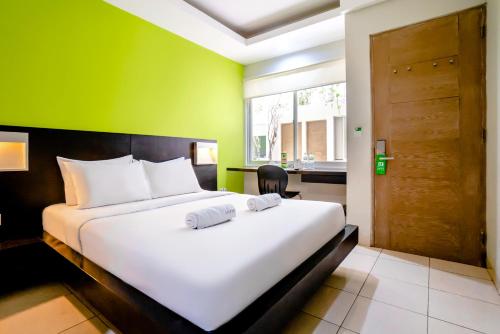 - une chambre avec un lit blanc et un mur vert dans l'établissement LeGreen Suite Pejompongan, à Jakarta