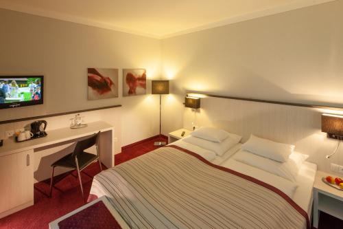 a hotel room with a television and a bed at Bergers Airporthotel Memmingen in Memmingerberg