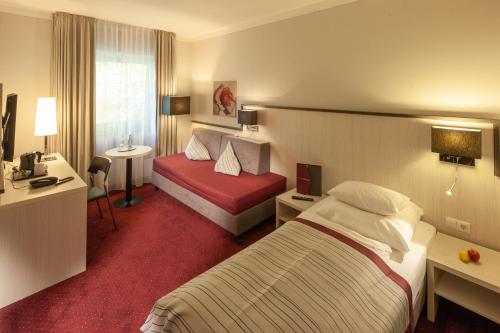 a hotel room with two beds and a desk at Bergers Airporthotel Memmingen in Memmingerberg