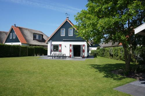 a white house with a black roof and a yard at Buitenplaats Villa Deluxe in Callantsoog