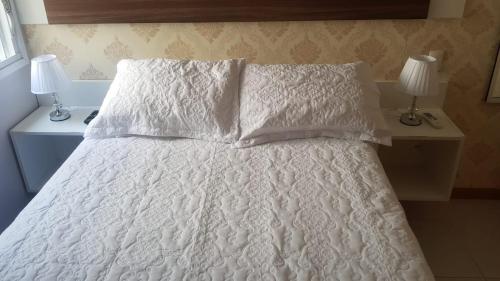 a bed with a white comforter and two lamps at Excelente Apartamento Alto Padrão Centro Ed Dubai in Capão da Canoa