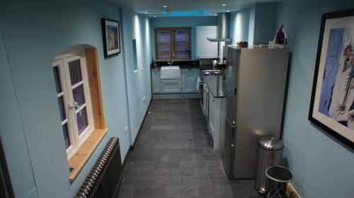 a kitchen with blue walls and a hallway with a refrigerator at Simpsons Cottage - Grove Road Cottages in Stratford-upon-Avon