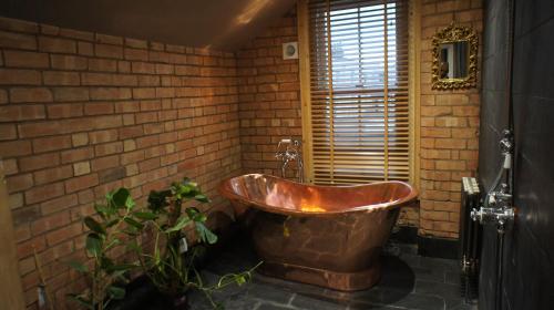 une baignoire en cuivre dans une salle de bains en brique avec une plante dans l'établissement Simpsons Cottage - Grove Road Cottages, à Stratford-upon-Avon